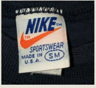 Vintage Nike orange tag with orange swoosh and blue lettering on a light label