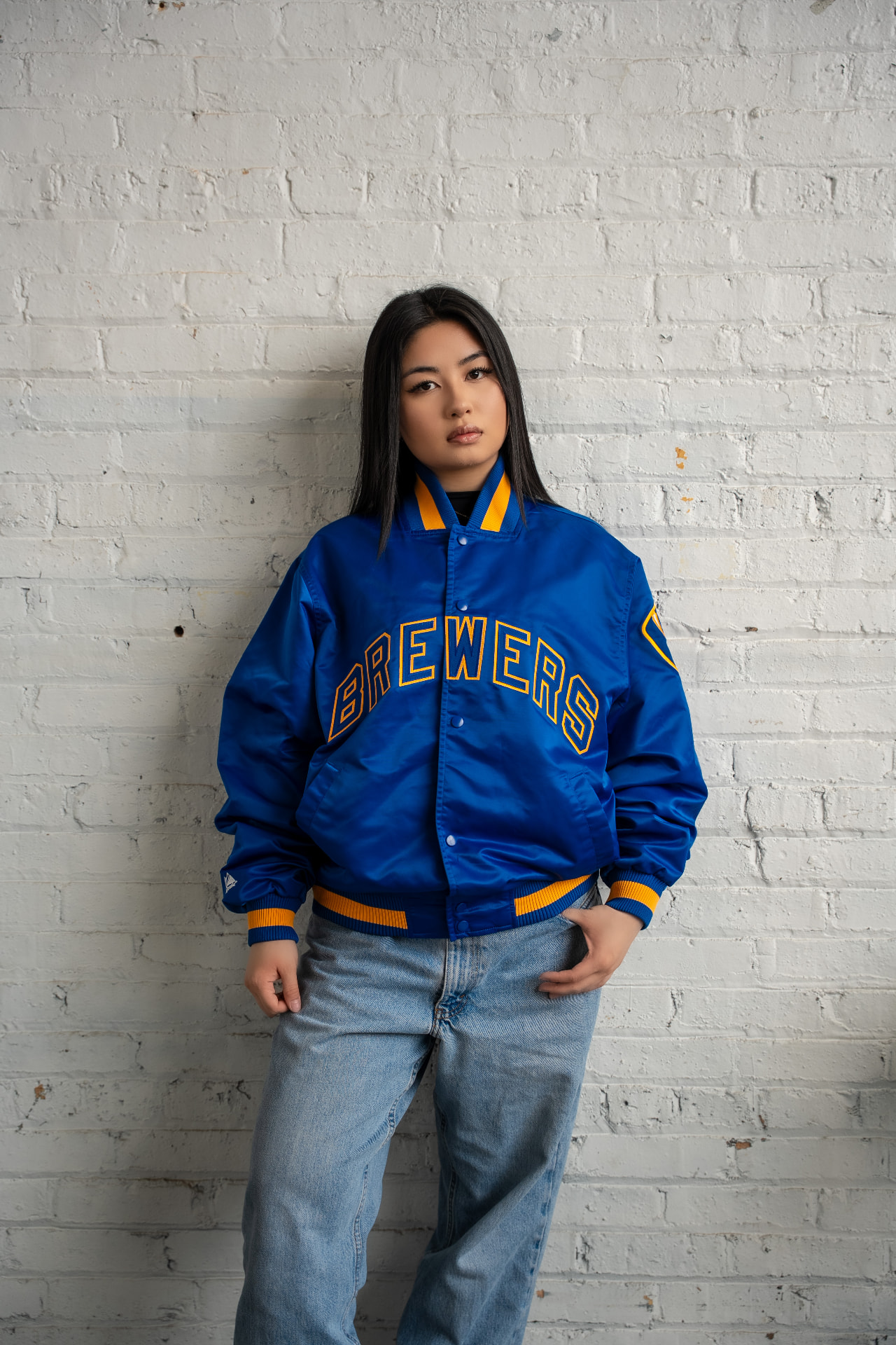 Vintage satin Brewers jacket styled with light-wash denim against a white brick wall